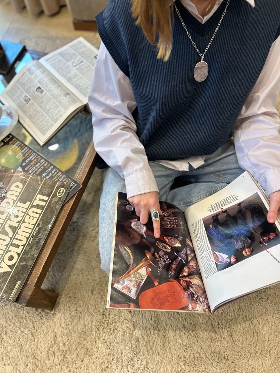 Manos con anillo y dije, hojeando una revista vintage.